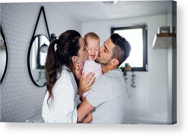 Toddler Acrylic Print featuring the photograph Portrait of young couple with toddler girl in the morning indoors in bathroom at home, kissing. by Halfpoint Images