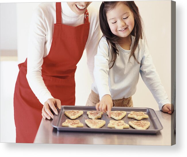 Mid Adult Women Acrylic Print featuring the photograph Young Girl Stands With Her Mum by the Kitchen Counter, Choosing a Christmas Cookie From a Baking Tray by Digital Vision.