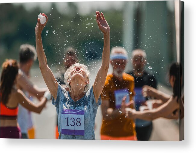 Mature Adult Acrylic Print featuring the photograph Senior marathon runner refreshing herself with water during a race. by Skynesher