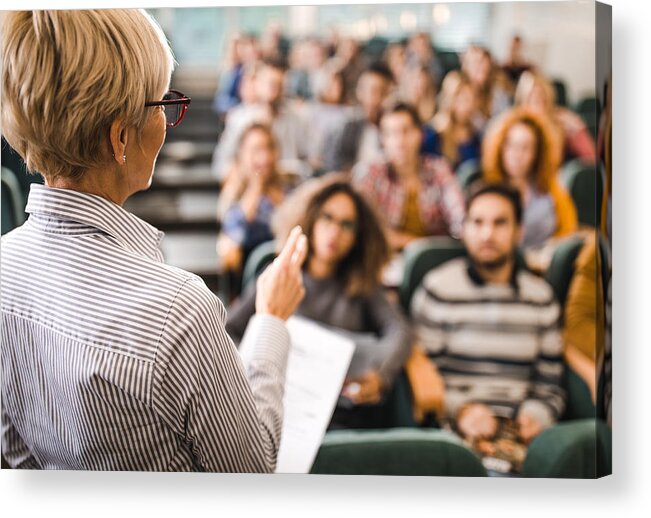 Working Acrylic Print featuring the photograph Rear view of mature teacher giving a lecture in a classroom. by Skynesher