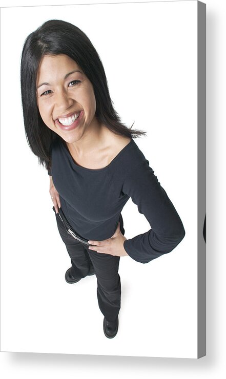 White Background Acrylic Print featuring the photograph Young Attractive Asian Woman Dressed In Black Puts Her Hands On Her Hips And Smiles Up To The Camera by Photodisc