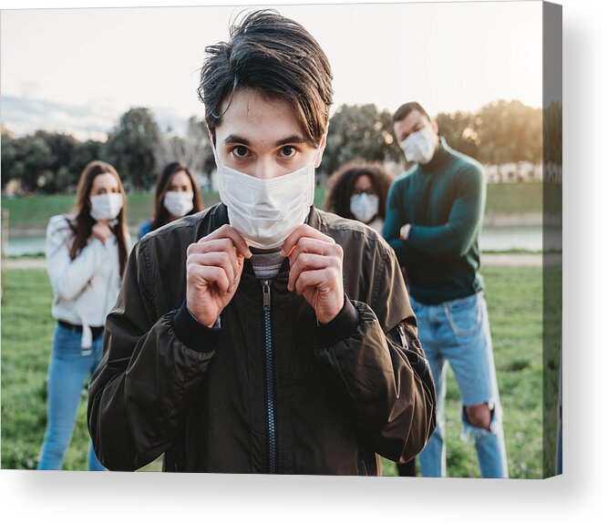 Air Pollution Acrylic Print featuring the photograph Young adult man wearing a pollution mask to protect himself from viruses. His friends are in the background. #2 by FilippoBacci