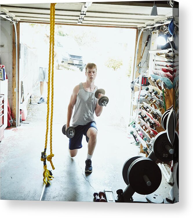Young Men Acrylic Print featuring the photograph Young man doing lunges with dumbbells in gym in garage by Thomas Barwick