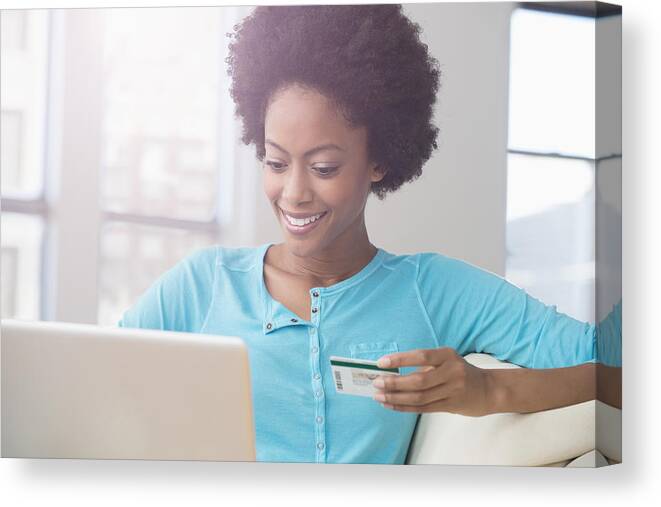 Debt Canvas Print featuring the photograph African American woman shopping on laptop with credit card on sofa by Jose Luis Pelaez Inc