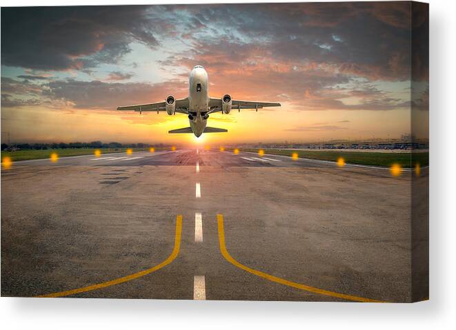Taking Off Canvas Print featuring the photograph Airplane taking off from the airport runway in beautiful sunset light by Issarawat Tattong