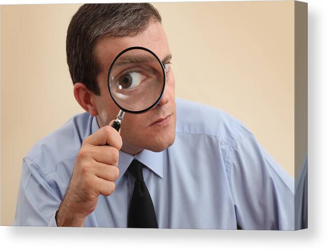 Expertise Canvas Print featuring the photograph Businessman looking at camera through a magnifying glass by Mgkaya
