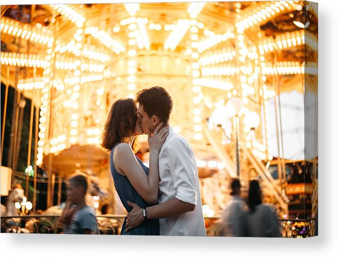 Young Men Canvas Print featuring the photograph Couple kissing near the marry-go-round in the park by Igor Ustynskyy