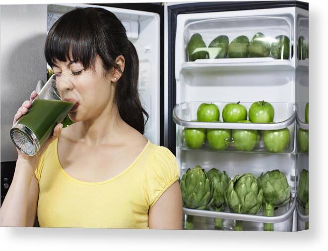 Vitamin C Canvas Print featuring the photograph Grimacing mixed race woman drinking healthy drink near refrigerator by Jill Giardino