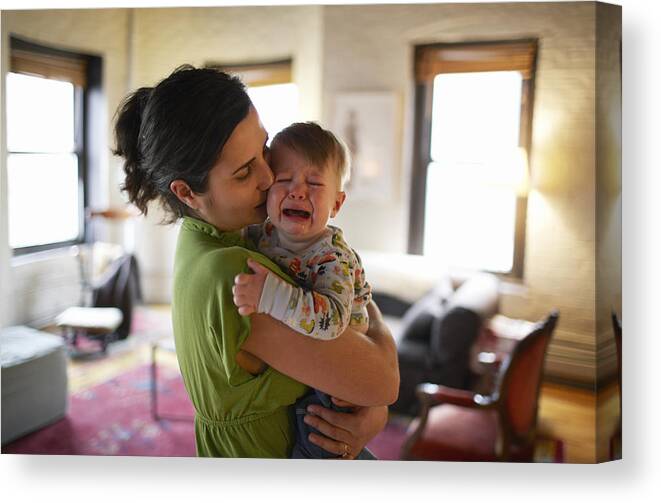 Three Quarter Length Canvas Print featuring the photograph Mother holding and kissing crying baby boy (12-17 months) (focus on foreground) by Ben Bloom