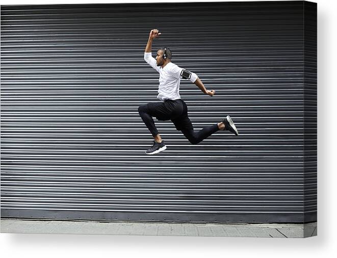 Young Men Canvas Print featuring the photograph Sporty young man jumping against shutter by Morsa Images