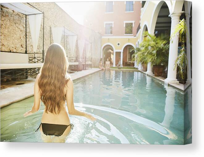 Spa Canvas Print featuring the photograph Woman wading into pool in courtyard of hotel while friends sit on edge by Thomas Barwick