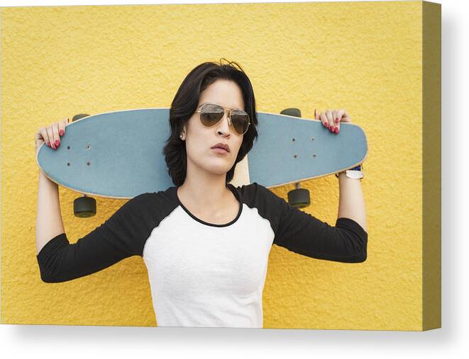 Toughness Canvas Print featuring the photograph Young Hispanic woman standing near yellow wall with skateboard by Tony Anderson