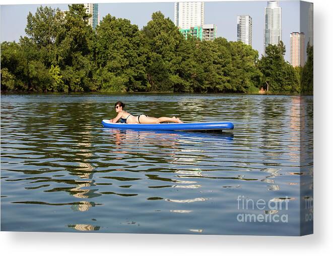 Woman Canvas Print featuring the photograph A female stand up paddle board lounges on the crystal clear blue waters of on Lady Bird Lake in Austin, Texas- Stock Image by Dan Herron