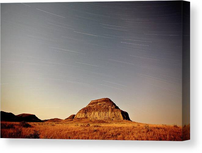 Castle Butte Canvas Print featuring the digital art Moon lit Castle Butte and star tracks in scenic Saskatchewan by Mark Duffy