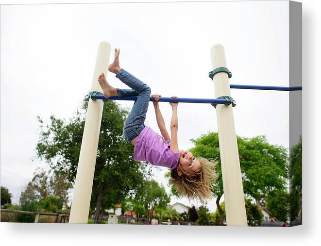 Girl Canvas Print featuring the photograph Playful Girl Hanging Upside Down On Monkey Bars At Playground Against Clear Sky by Cavan Images