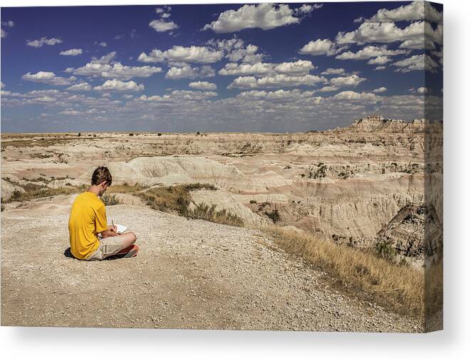 Badlands Canvas Print featuring the photograph Teen Boy Writes In Notebook Overlooking Badlands National Park, Usa by Cavan Images