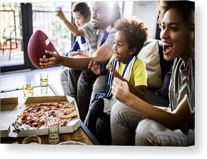 Unhealthy Eating Canvas Print featuring the photograph Cheerful black family cheering while watching rugby match on TV at home. by Skynesher