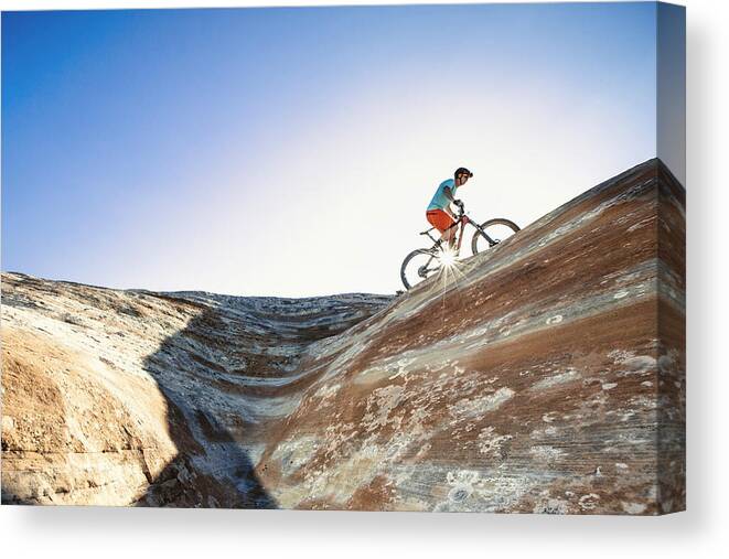 People Canvas Print featuring the photograph A man riding a mountain bike on an extreme sandstone ledge by Robb Reece