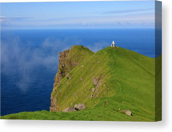 Scenics Canvas Print featuring the photograph A small lighthouse on top of a grassy steep cliff high above the sea by Rainer Grosskopf