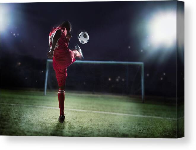 Young Men Canvas Print featuring the photograph Athlete kicking soccer ball into a goal by FangXiaNuo