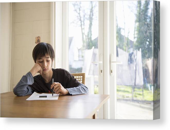 Working Canvas Print featuring the photograph Boy sitting at table, holding pen to paper by Kaori Ando
