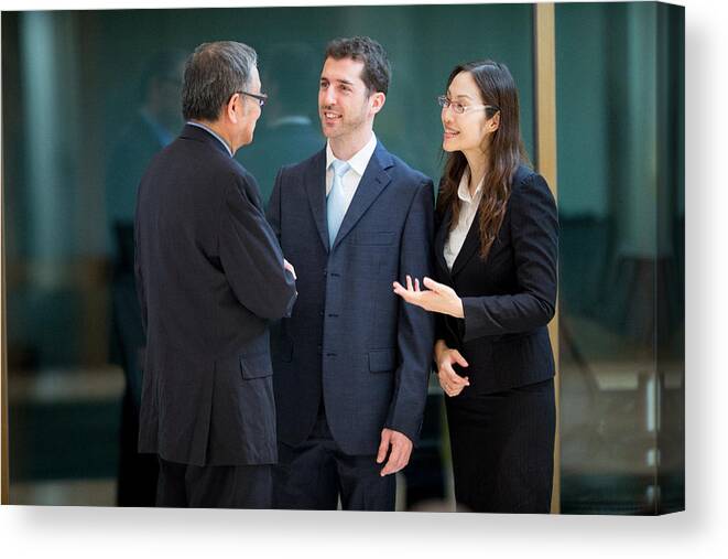 Corporate Business Canvas Print featuring the photograph Caucasian businessman with his interpreter discussing a deal with senior Asian businessman by Casarsa