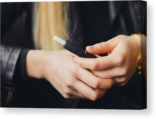 White People Canvas Print featuring the photograph Close up electronic cigarette with case and blur girl on background by SHipskyy