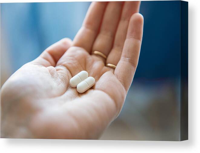 Problems Canvas Print featuring the photograph Close-up view of a hand holding two white pills in the palm above a blurry background, painkiller by Oleksandra Troian