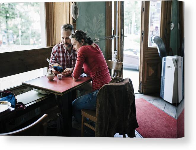 Heterosexual Couple Canvas Print featuring the photograph Couple in Cafe reading Tour Guide by Hinterhaus Productions