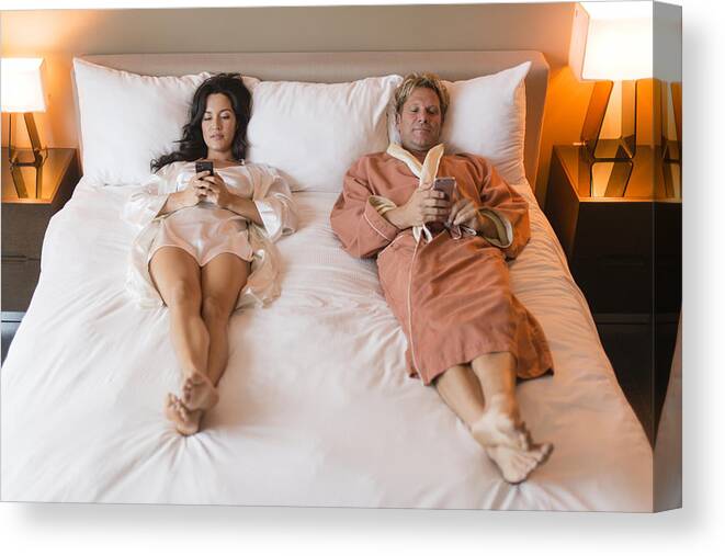 Heterosexual Couple Canvas Print featuring the photograph Couple using cell phones on bed by Rick Gomez