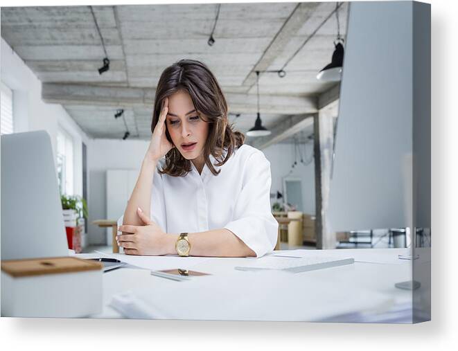 Working Canvas Print featuring the photograph Female entrepreneur with headache sitting at desk by Izusek