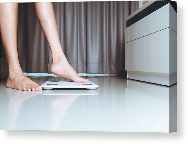 Working Canvas Print featuring the photograph Female leg is stepping on white scales at home by Pornchai Soda