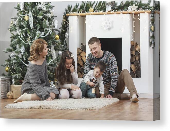 Mid Adult Men Canvas Print featuring the photograph Happy family sitting on rug by Christmas tree at home by Vasily Pindyurin