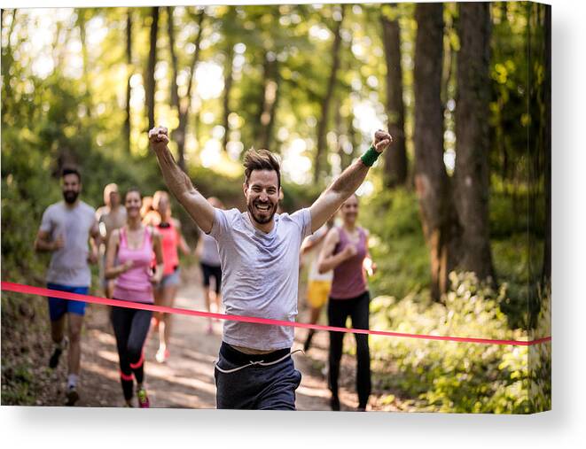 Young Men Canvas Print featuring the photograph Happy marathon runner winning and crossing finish line with arms raised. by Skynesher