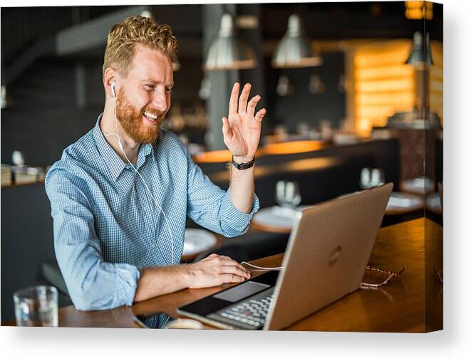 Young Men Canvas Print featuring the photograph Happy young businessman waving to an online client. by DjelicS