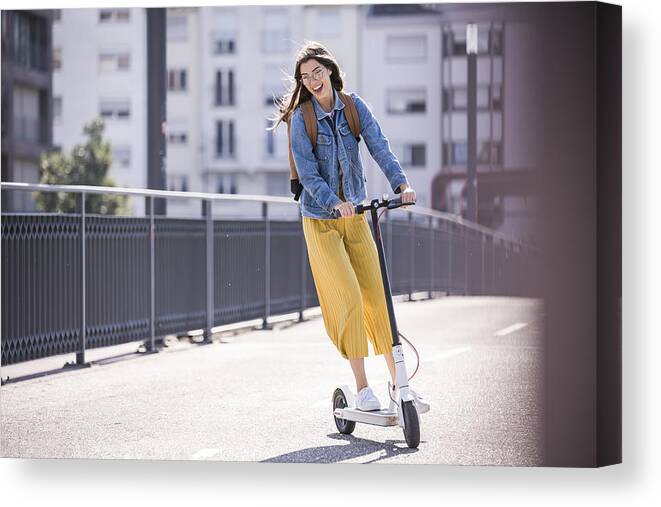 Environmental Conservation Canvas Print featuring the photograph Happy young woman riding electric scooter on a bridge by Westend61