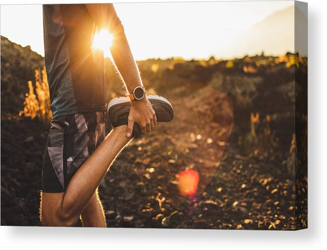 Scenics Canvas Print featuring the photograph Male runner stretching leg and feet and preparing for running outdoors. Smart watch or fitness tracker on hand. Beautiful sun light on background. Active and healthy lifestyle concept. by Olegbreslavtsev