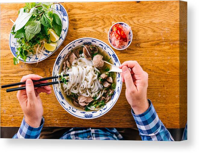 People Canvas Print featuring the photograph Man eating Vietnamese Pho soup with noodles and beef, personal perspective view by Alexander Spatari