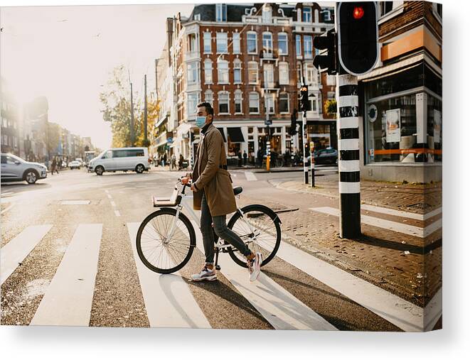 Working Canvas Print featuring the photograph Man with face mask pushing bicycle in the city during coronavirus pandemic lockdown by Drazen_