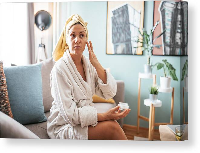 Tranquility Canvas Print featuring the photograph Mature woman applies face moisturizer and beauty mask on her face by Drazen_