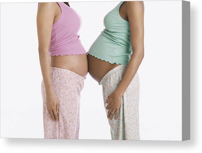 Mid Adult Women Canvas Print featuring the photograph Mid Section of Two Pregnant Women in Pajamas Standing Face to Face, Their Stomachs Touching by Nancy Ney