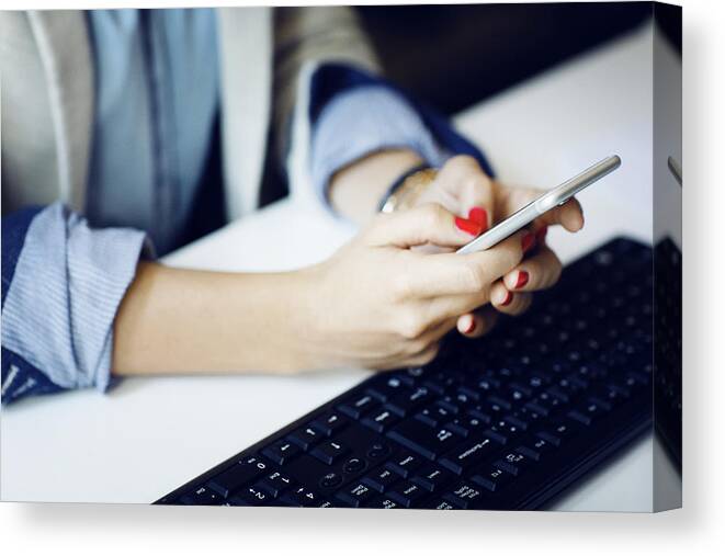 Expertise Canvas Print featuring the photograph Midsection of businesswoman using phone by keyboard at desk by Cavan Images