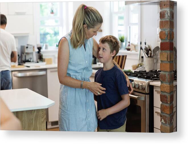 Domestic Room Canvas Print featuring the photograph Mother comforting son in home kitchen. by Martinedoucet