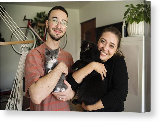 Pets Canvas Print featuring the photograph Portrait of millennial couple and newly adopted kitten at home. by Martinedoucet
