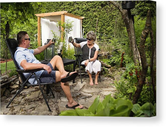 Heterosexual Couple Canvas Print featuring the photograph Senior couple having a drink in backyard. by Martinedoucet