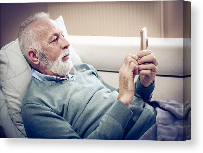 Domestic Room Canvas Print featuring the photograph Senior man using smart phone. by Mladen Zivkovic