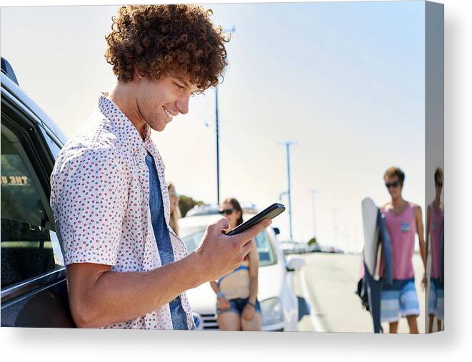 Young Men Canvas Print featuring the photograph Smiling young man at a car checking his cell phone by Westend61