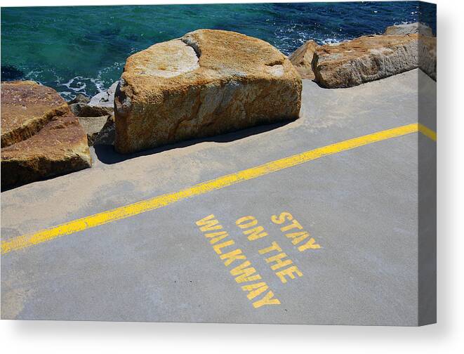 Water's Edge Canvas Print featuring the photograph 'Stay on the Walkway' sign stencilled in yellow paint on the concrete walkway of the Southern Break Wall at Coffs Harbour, New South Wales, Australia by Simon McGill
