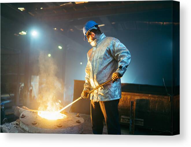 Working Canvas Print featuring the photograph Steel worker in protective clothing raking furnace in an industry by RainStar