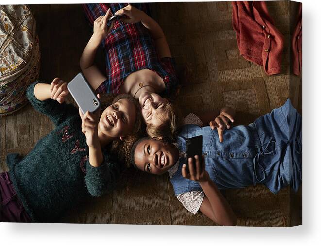 Adolescence Canvas Print featuring the photograph Top view of 3 tween girls laughing and looking at their smartphones by Klaus Vedfelt